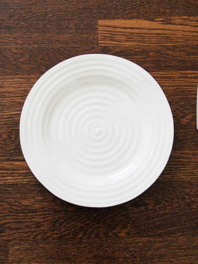 An empty white plate sits on a wood table with a fork and knife to either side